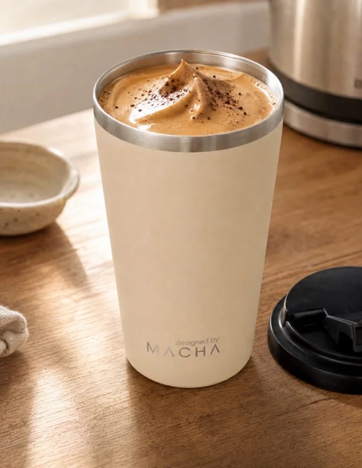A dalgona whipped over milk in the MACHA Cup in Milk, lid off beside it on a wooden bench