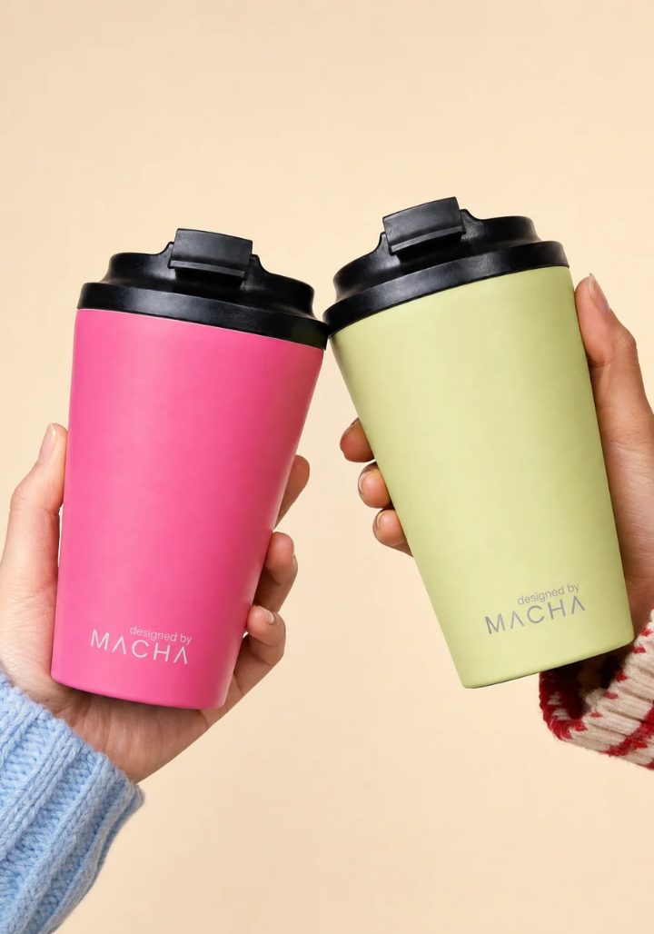 Two MACHA Cups held up side by side against a cream backdrop, one pink and one pale green