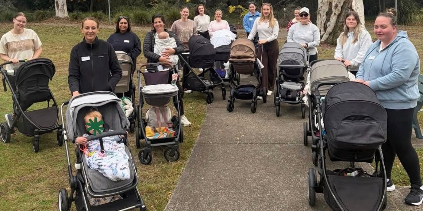 A group of mothers standing with their prams on a park path, facing the camera