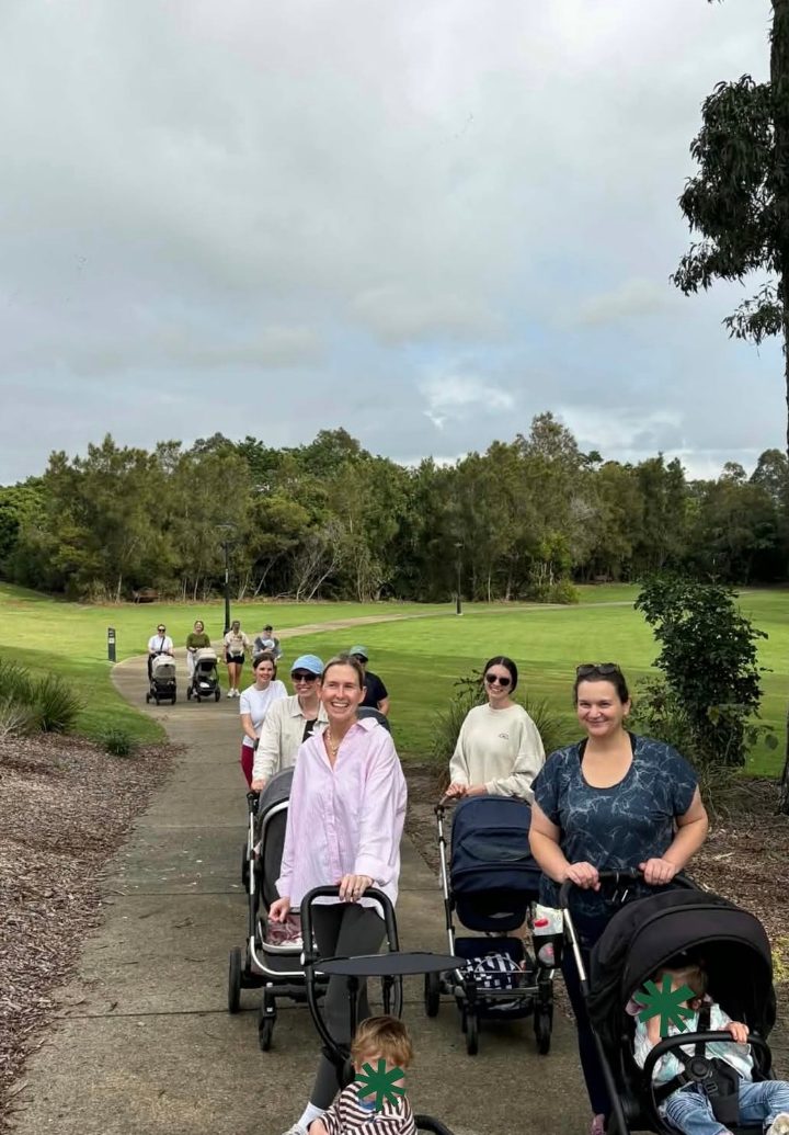 Mothers walking in single file along a park path with their prams